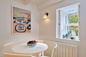 Ein Essbereich mit einem runden Tisch, weißen Stühlen, einer Schale Kiefernzapfen und einem Gemälde an der Wand.