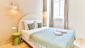A neatly made bed with a green throw, a bedside lamp, and a window with curtains. - Studio 15m² avec clim – Pratique et fonctionnel (Le Pré-Saint-Gervais)