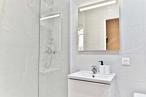 A modern bathroom with a glass shower enclosure, a white sink with a faucet, and a mirror above the sink. - Studio 15m² avec clim – Pratique et fonctionnel (Le Pré-Saint-Gervais)