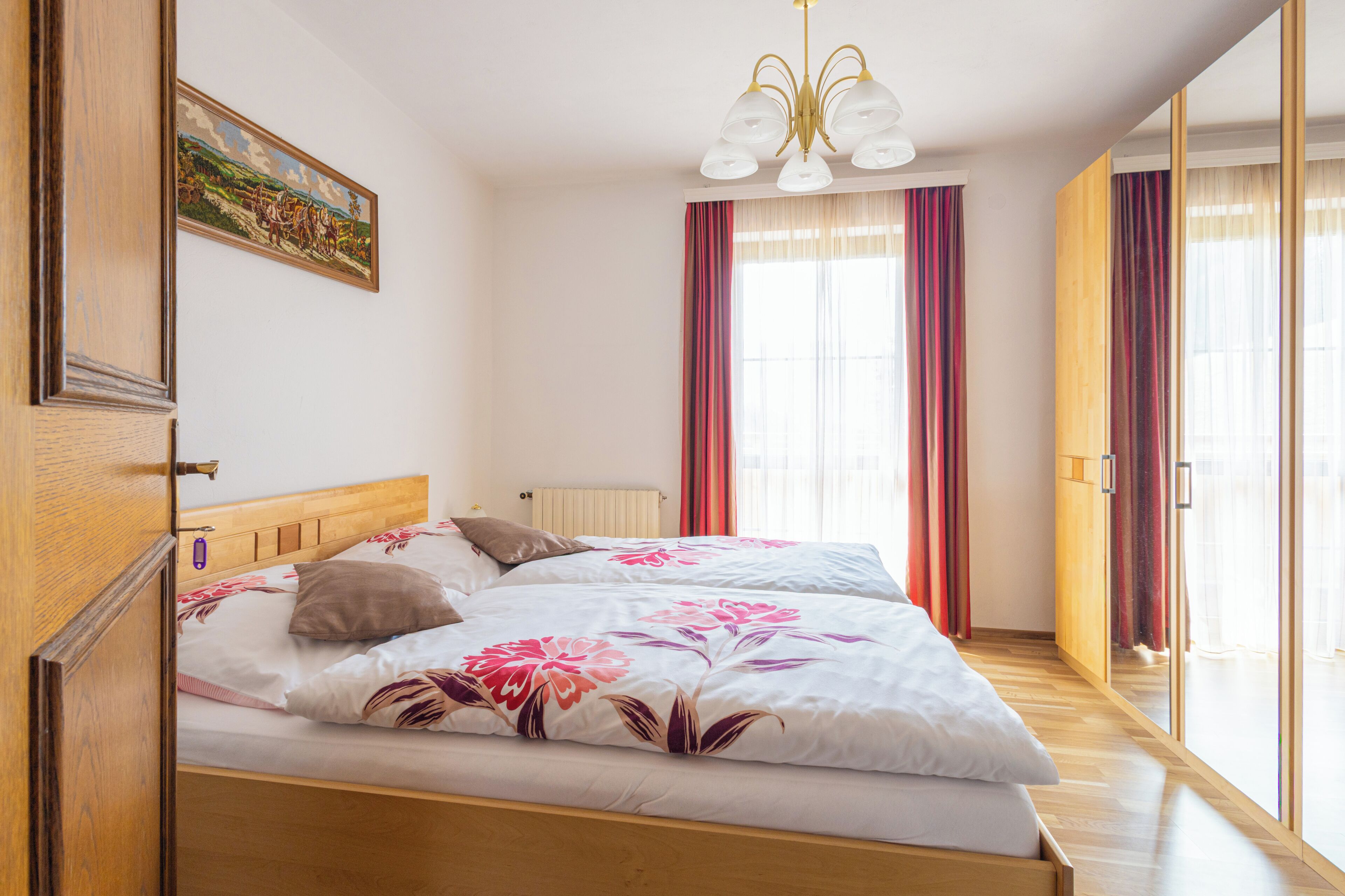 Ein Schlafzimmer mit einem hölzernen Bett, einem Bild an der Wand und einem großen Fenster mit Vorhängen.