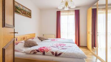 Ein Schlafzimmer mit einem hölzernen Bett, einem Bild an der Wand und einem großen Fenster mit Vorhängen.