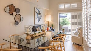 Una sala de estar moderna con una mesa de comedor de vidrio, sillas de madera, un sofá y un ventanal con persianas.