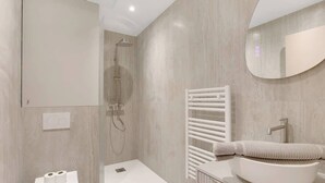 Casa de banho moderna com chuveiro, sanita e lavatório.