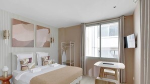 Quarto de hotel moderno com uma cama grande, mesa de cabeceira e televisão na parede.