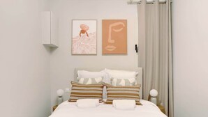 A neatly made bed with striped pillows, a white headboard, and two framed artworks on the wall. - Air-conditioned studio offering comfort and elegance (Neuilly-sur-Seine)