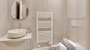 A modern bathroom with a round mirror, a vessel sink, a towel rack, and a toilet. - Air-conditioned studio offering comfort and elegance (Neuilly-sur-Seine)