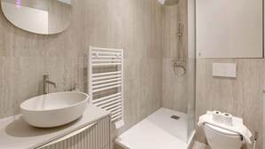 Un baño moderno con un lavamanos ovalado grande, un perchero, una ducha y un inodoro.