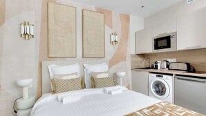 Una habitación de hotel moderna con una cama bien hecha, una lavadora, un microondas y una kitchenette pequeña.