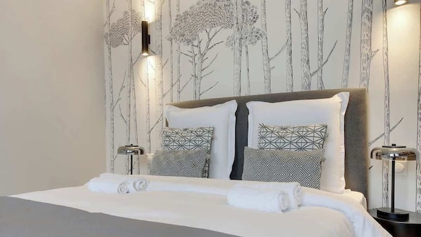 Et moderne hotelværelse med en stor seng, geometrisk mønstrede puder og en væg med et træmotiv.