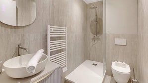 Et moderne badeværelse med en stor, oval håndvask, et brusebadeværelse og et toilet.