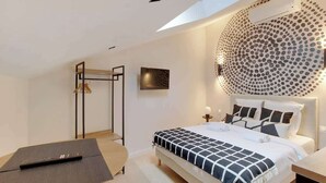 A modern bedroom with a bed, a standing desk, a TV, and a unique circular wall design. - Studio climatisé intimiste – Neuilly (Neuilly-sur-Seine)