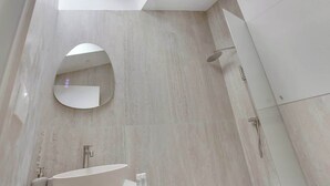 A modern bathroom with a skylight, a round mirror, a freestanding bathtub, and a shower. - Studio climatisé intimiste – Neuilly (Neuilly-sur-Seine)
