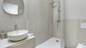 A modern bathroom with a large oval sink, a round mirror, and a shower area. - Studio climatisé intimiste – Neuilly (Neuilly-sur-Seine)
