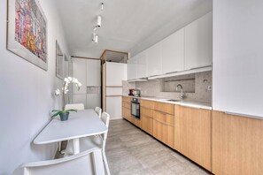 Eine moderne Küche mit weißen Schränken, einer Marmorarbeitsplatte und einem Essbereich mit einem weißen Tisch und Stühlen.
