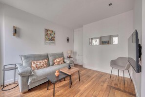 Ein modernes Wohnzimmer mit grauem Sofa, einem kleinen Tisch, einem Sessel und Holzboden.
