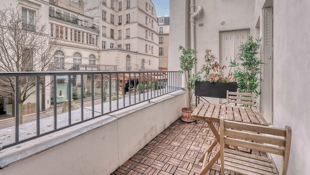 Un balcon avec un banc en bois, des plantes en pot et une vue sur les bâtiments voisins.