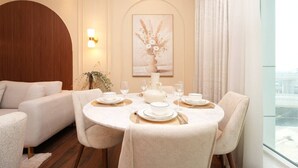 Zona pranzo con tavolo rotondo apparecchiato per quattro persone, un divano e un'ampia finestra con tende.
