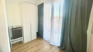 A room with a wooden floor, a white wardrobe, and a television on a stand.