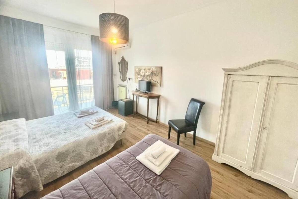 A hotel room with two beds, a desk, a chair, a wardrobe, and a hanging light fixture.