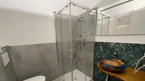 A modern bathroom with a glass-enclosed shower, a white toilet, and a vanity with a decorative bowl sink.