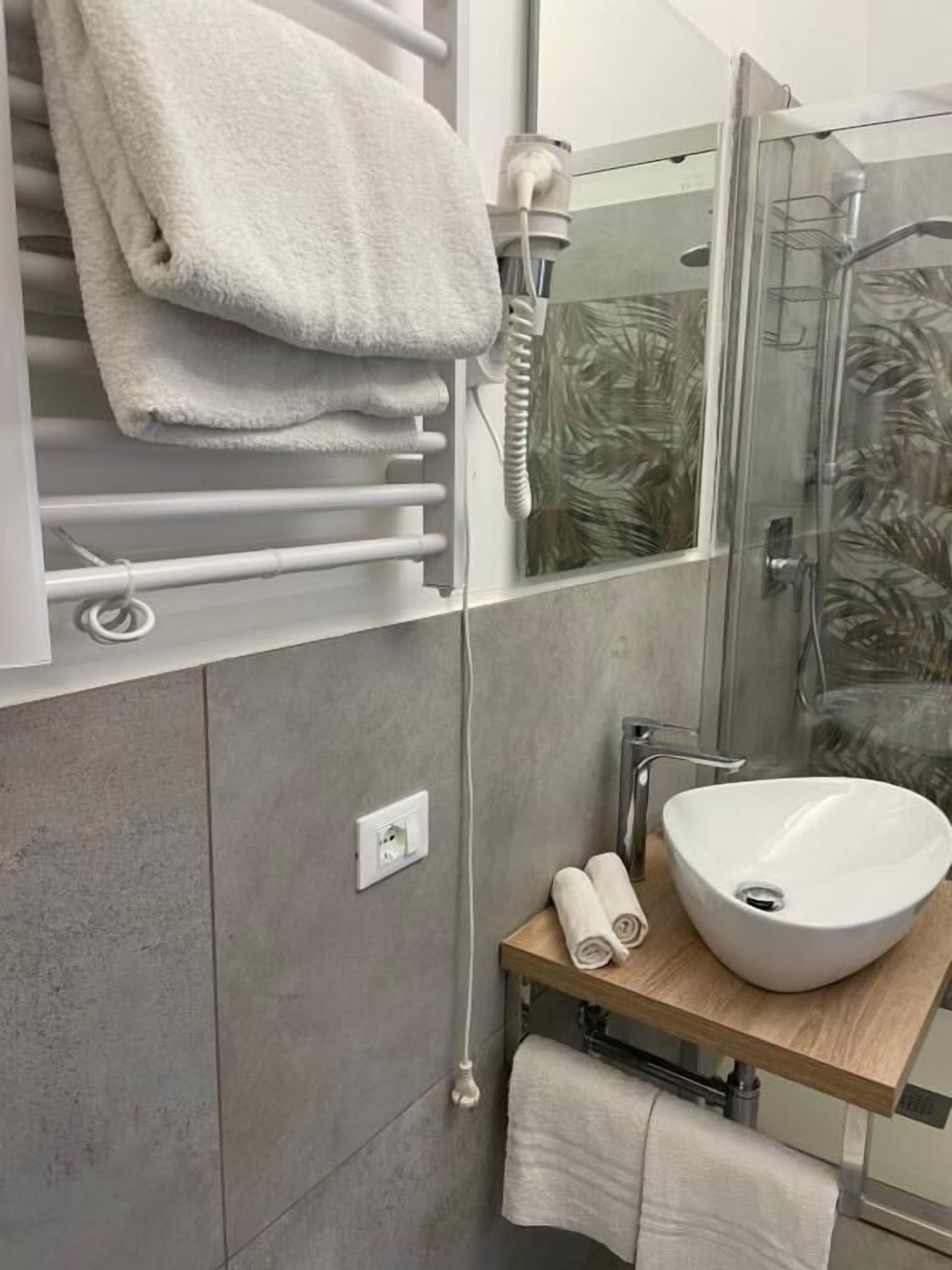 A modern bathroom with a glass shower enclosure, a white sink, and a towel rack.