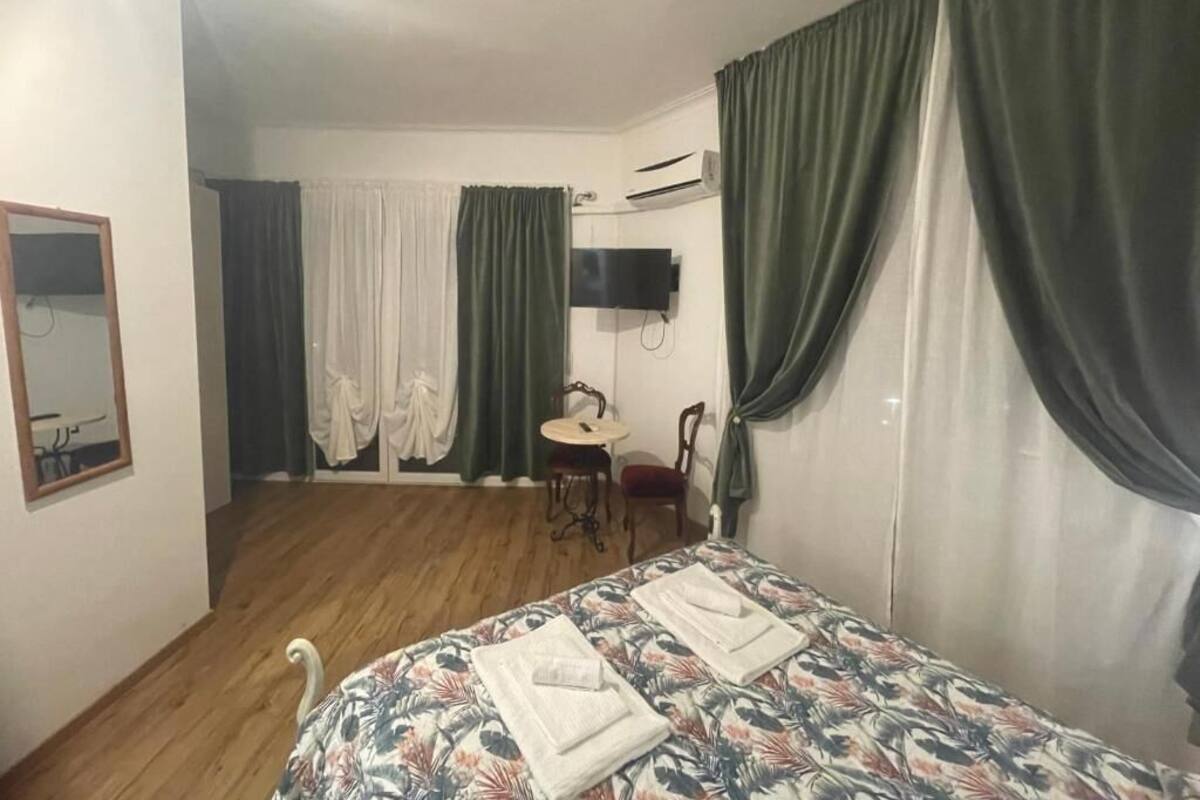 A hotel room with a bed, a small table with chairs, a TV mounted on the wall, and curtains.
