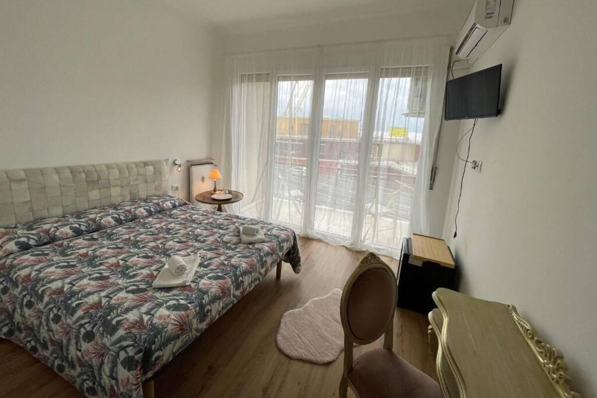 A hotel room with a bed, a chair, a desk, a TV, and a window with curtains.
