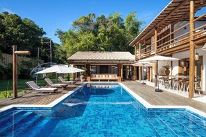 Ein Swimmingpool mit Liegestühlen und Sonnenschirmen, ein Holzdeck und ein Gebäude mit einem Ziegeldach.
