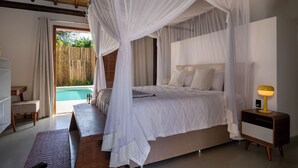 A bedroom with a four-poster bed, a bedside table with a lamp, and a view of a swimming pool. - Casa Villamar25 (Porto Seguro)