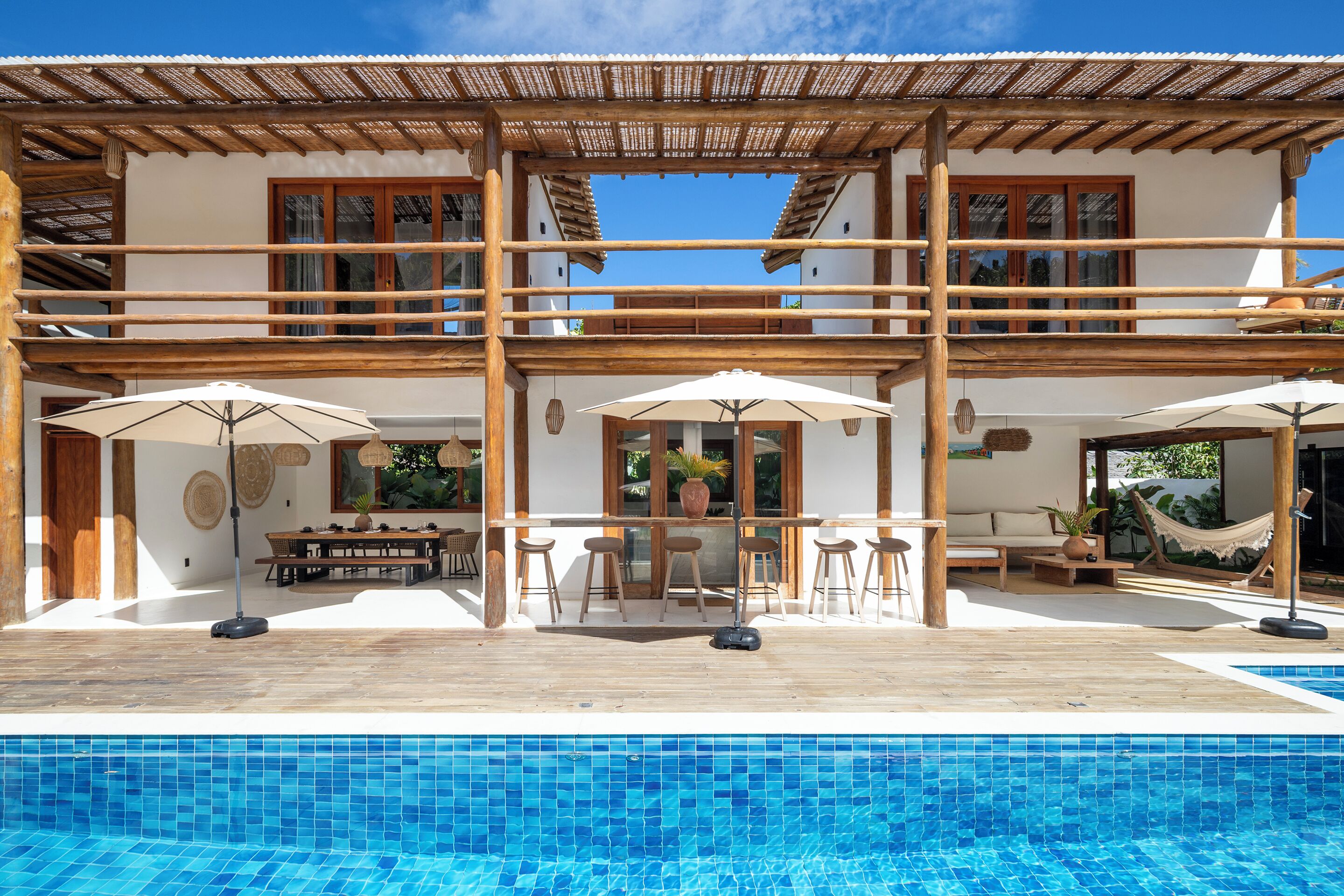 Ein zweistöckiges Gebäude mit Pool, Holzterrasse und Sitzgelegenheit im Freien.