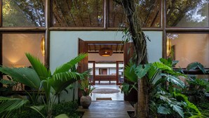 A wooden pathway leading to a traditional-style building with large windows and indoor plants. - Casa Villamar25 (Porto Seguro)