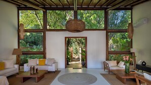 A spacious living room with large windows, a central rug, and a view of a garden. - Casa Villamar25 (Porto Seguro)