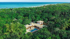 A modern house with a pool surrounded by dense tropical vegetation and a beach in the background. - Casa Villamar25 (Porto Seguro)