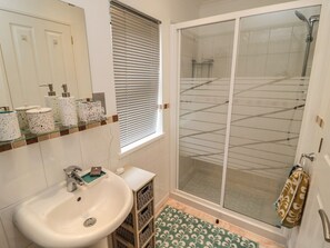 Een badkamer met een witte wastafel, een douchecabine met glazen wanden en een raam met zonwering.