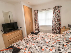Een slaapkamer met een bed, een televisie op een dressoir, een garderobe en een raam met gordijnen.