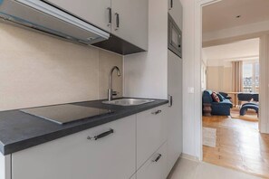 A modern kitchen with a black countertop, stainless steel sink, and white cabinets. - Élégant appartement 3 pièces avec balcon – Neuilly-sur-Seine (Neuilly-sur-Seine)