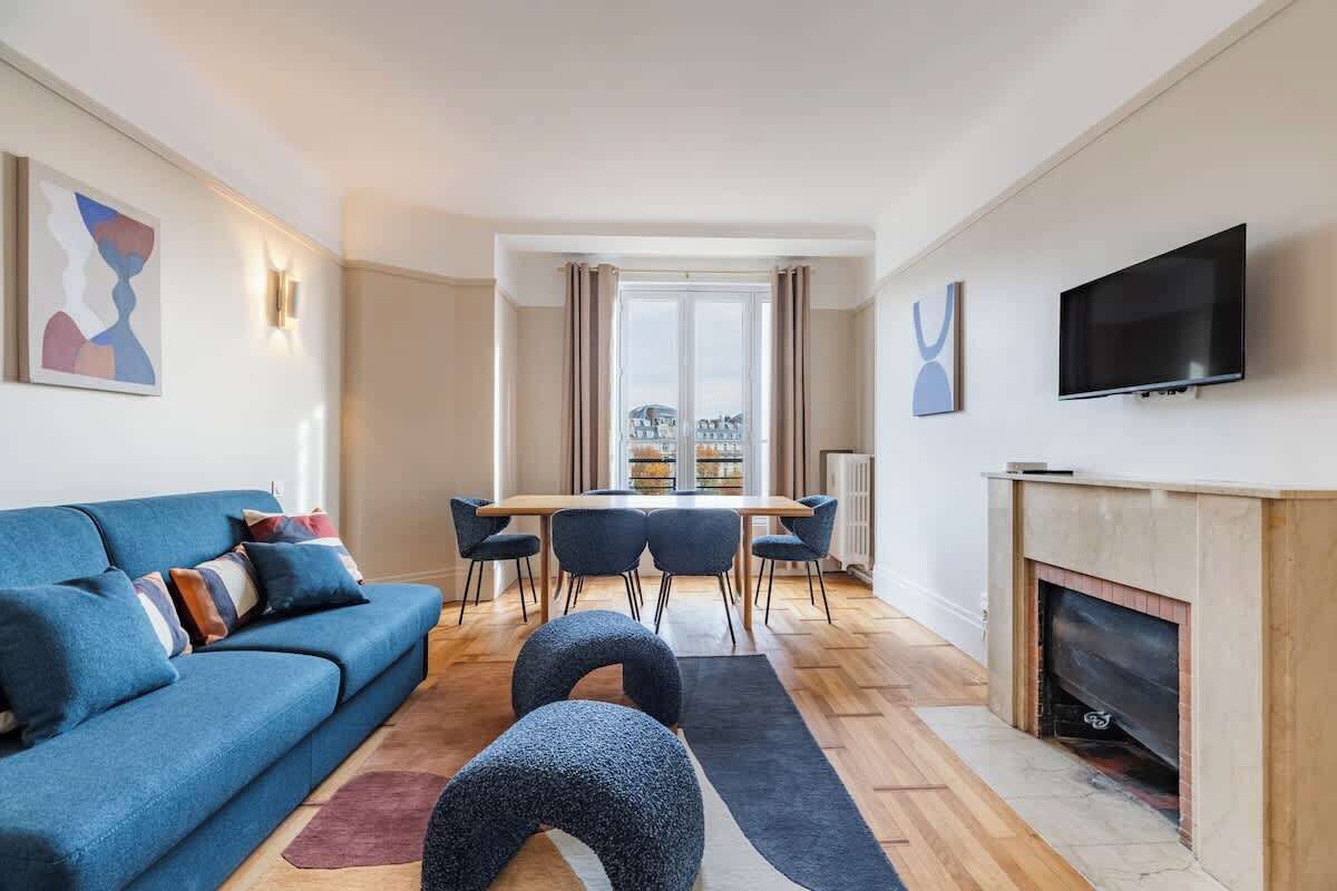 Un salon moderne avec un canapé bleu, une table à manger avec des chaises, une cheminée et un téléviseur fixé au mur.