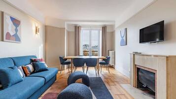 Un salon moderne avec un canapé bleu, une table à manger avec des chaises, une cheminée et un téléviseur fixé au mur.