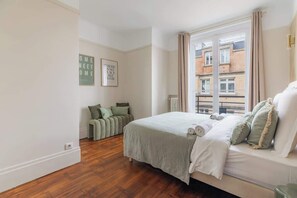 A bedroom with a bed, a window, and a green sofa. - Élégant appartement 3 pièces avec balcon – Neuilly-sur-Seine (Neuilly-sur-Seine)
