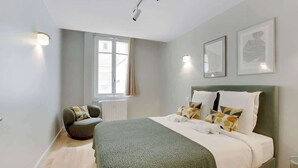 A modern bedroom with a large bed, a chair, and a window. - Elegant T2 in Neuilly-sur-Seine – Quiet & Comfortable (Neuilly-sur-Seine)