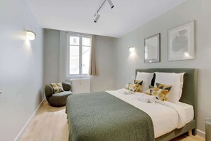 A modern bedroom with a large bed, a chair, and a window. - Elegant T2 in Neuilly-sur-Seine – Quiet & Comfortable (Neuilly-sur-Seine)