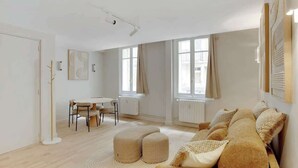 A modern living room with a sofa, ottomans, a dining table, and chairs. - Elegant T2 in Neuilly-sur-Seine – Quiet & Comfortable (Neuilly-sur-Seine)
