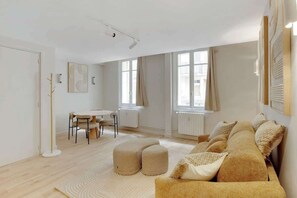 A modern living room with a sofa, ottomans, a dining table, and chairs. - Elegant T2 in Neuilly-sur-Seine – Quiet & Comfortable (Neuilly-sur-Seine)
