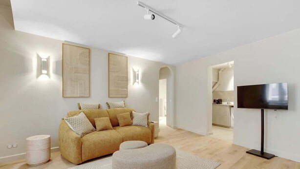 A modern living room with a sofa, ottoman, and a flat-screen TV. - Elegant T2 in Neuilly-sur-Seine – Quiet & Comfortable (Neuilly-sur-Seine)