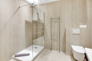 A modern bathroom with a glass shower enclosure, a white toilet, and a towel on the floor. - Elegant T2 in Neuilly-sur-Seine – Quiet & Comfortable (Neuilly-sur-Seine)