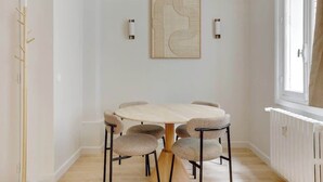 A dining area with a round table and six wicker chairs, a wall-mounted abstract art piece, and two wall sconces. - Elegant T2 in Neuilly-sur-Seine – Quiet & Comfortable (Neuilly-sur-Seine)
