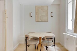 A dining area with a round table and six wicker chairs, a wall-mounted abstract art piece, and two wall sconces. - Elegant T2 in Neuilly-sur-Seine – Quiet & Comfortable (Neuilly-sur-Seine)