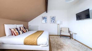 A modern hotel room with a large bed, a flat-screen TV, a chair, and two abstract paintings on the wall. - Studio fonctionnel et calme au cœur d'Issy (Issy-les-Moulineaux)