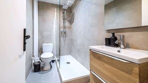 A modern bathroom with a glass-enclosed shower, a toilet, and a vanity with a mirror. - Studio fonctionnel et calme au cœur d'Issy (Issy-les-Moulineaux)