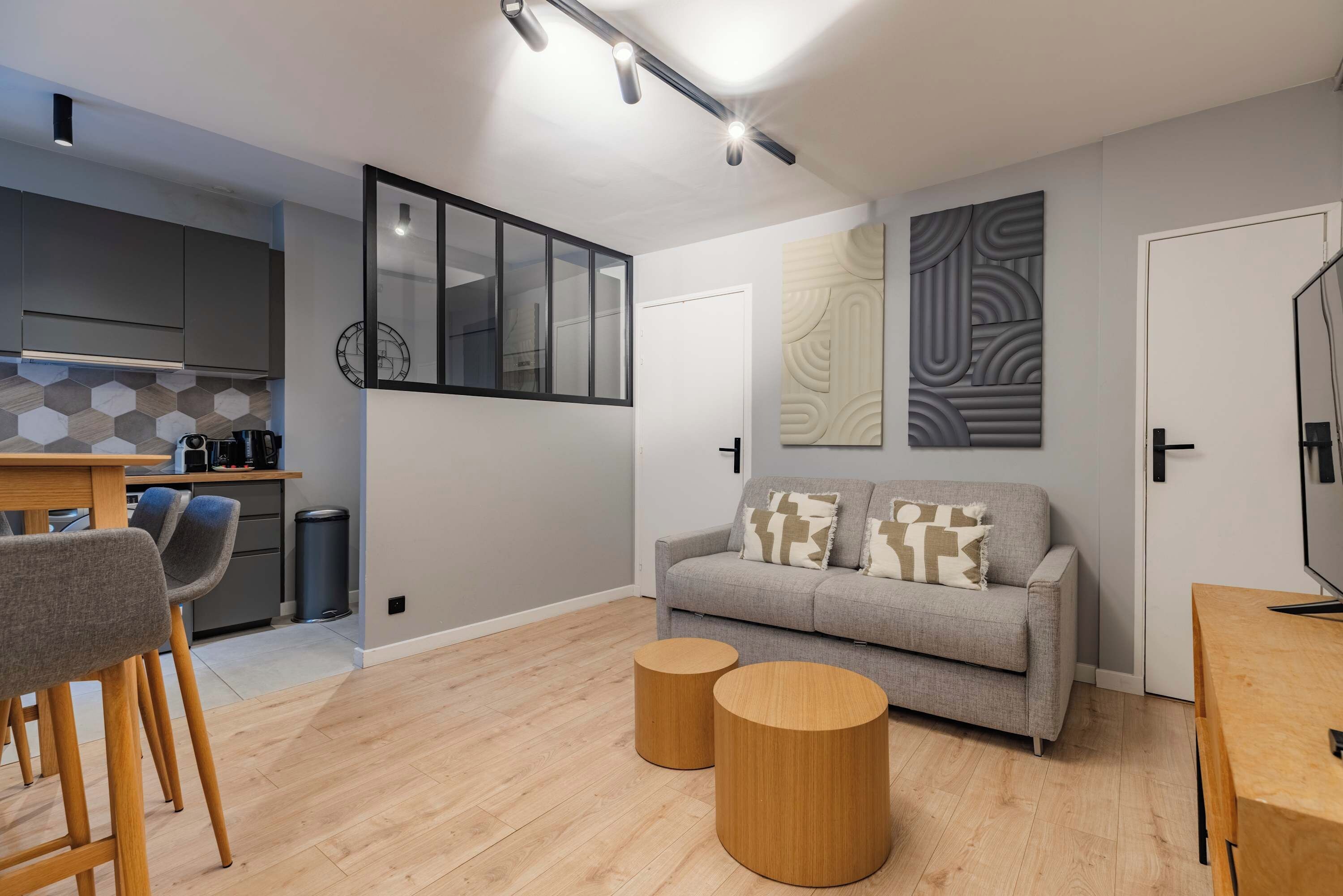 A modern living space with a grey sofa, wooden coffee table, and a kitchen area with a hexagonal tile backsplash.